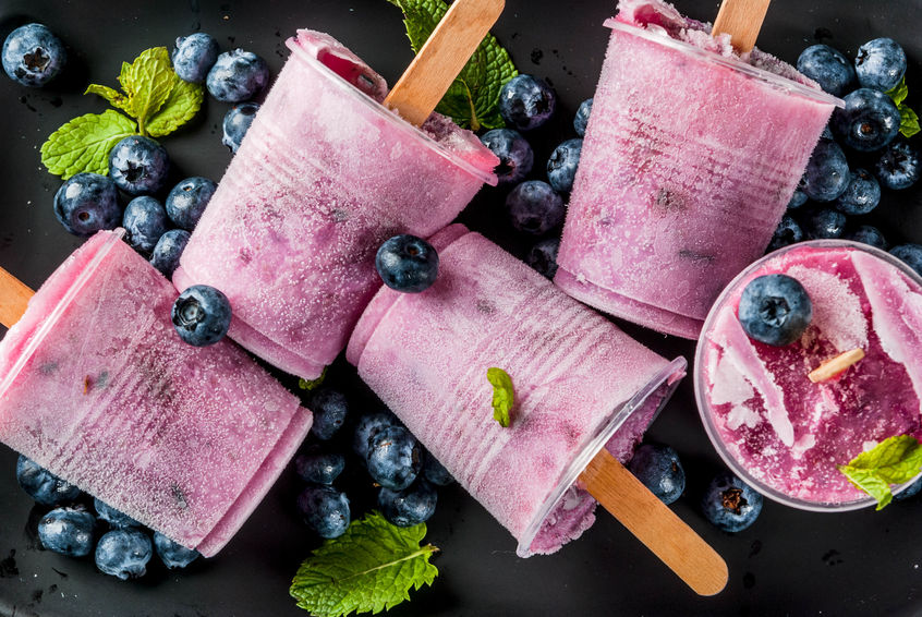 Summer desserts. Vegan food. Frozen drinks, smoothies. Ice cream popsicles from homemade Greek yogurt and fresh organic blueberries. With mint. On a plate, on a white marble table. Top view copy space